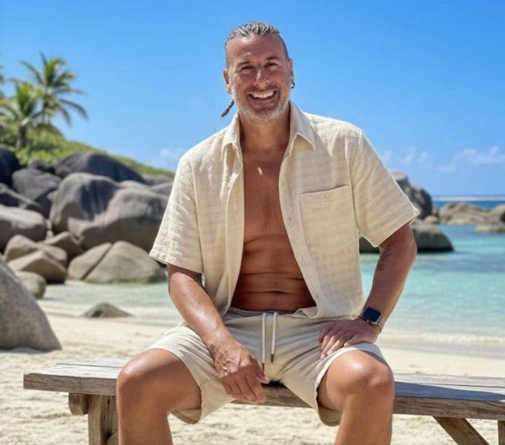 Ian Young smiling, sitting by the sea